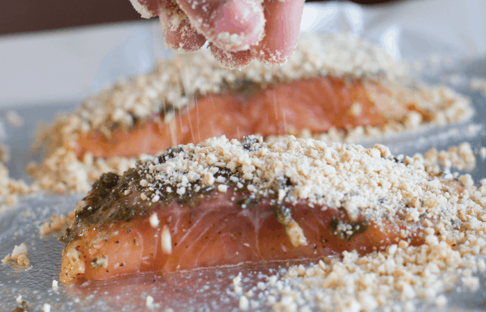 Hand sprinkling chopped cashews on salmon