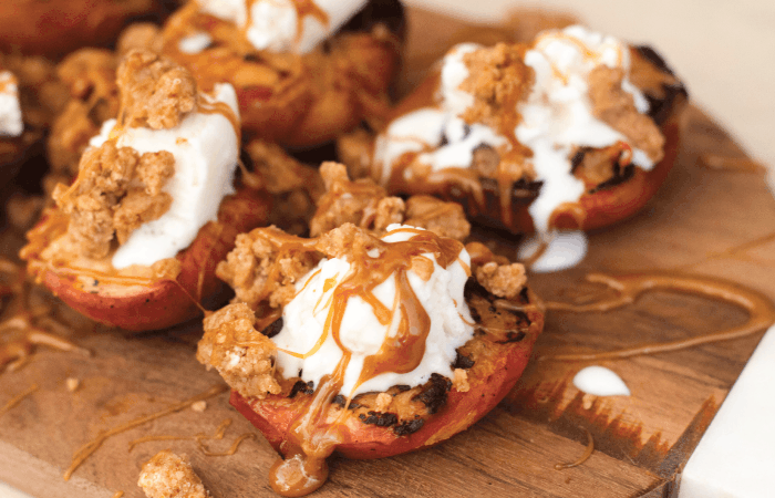 close up of Grilled Peaches topped with vanilla ice cream, Salted Caramel, and Toffee Crumble