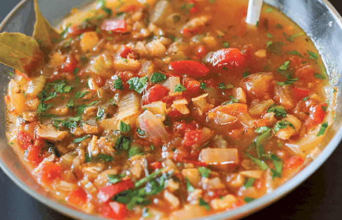 Close up of a glass bowl of Bermuda Inspired Fish Chowder with a spoon.