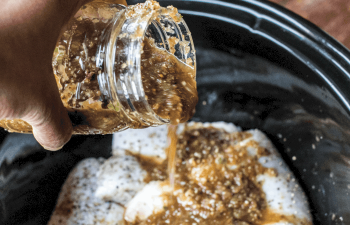 Pouring jerk marinade over chicken in slow cooker