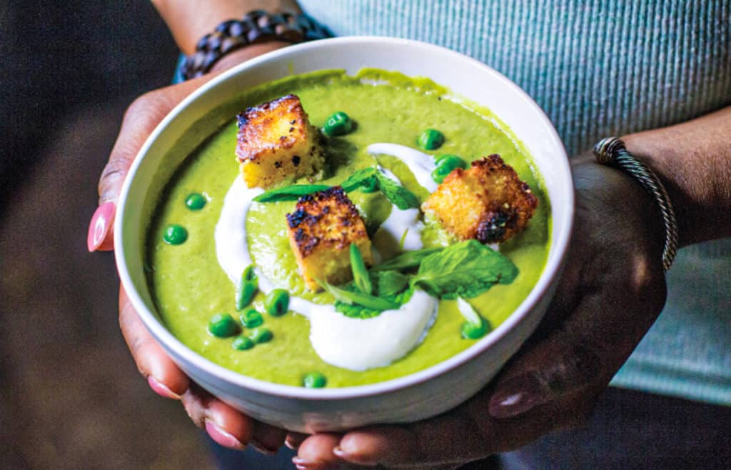 holding bowl of pea & mint soup with cornbread croutons