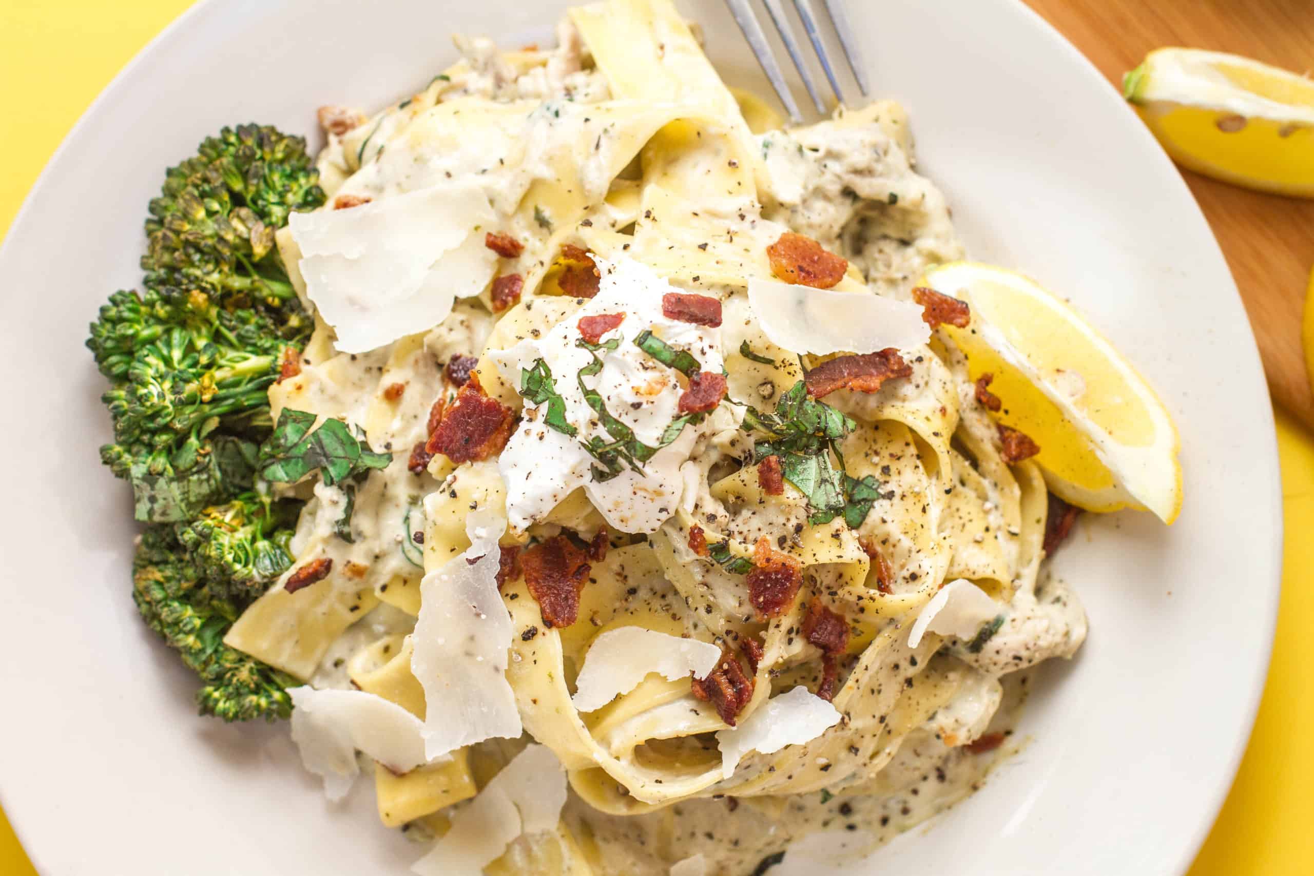 overhead shot of plated close up of creamy basil alfredo pappardelle with bacon pieces and Shaved Parmesan on top baby broccoli