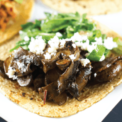 Close up of Chipotle Mushroom Tacos topped with crumbled queso fresco and mesclun greens.