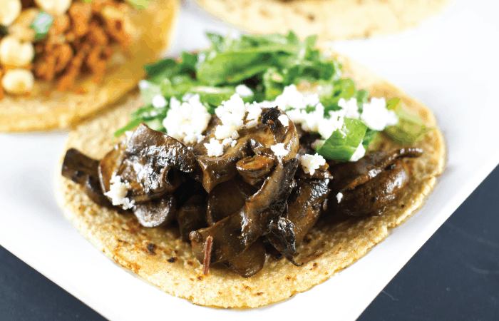 Close up of Chipotle Mushroom Tacos topped with crumbled queso fresco and mesclun greens.