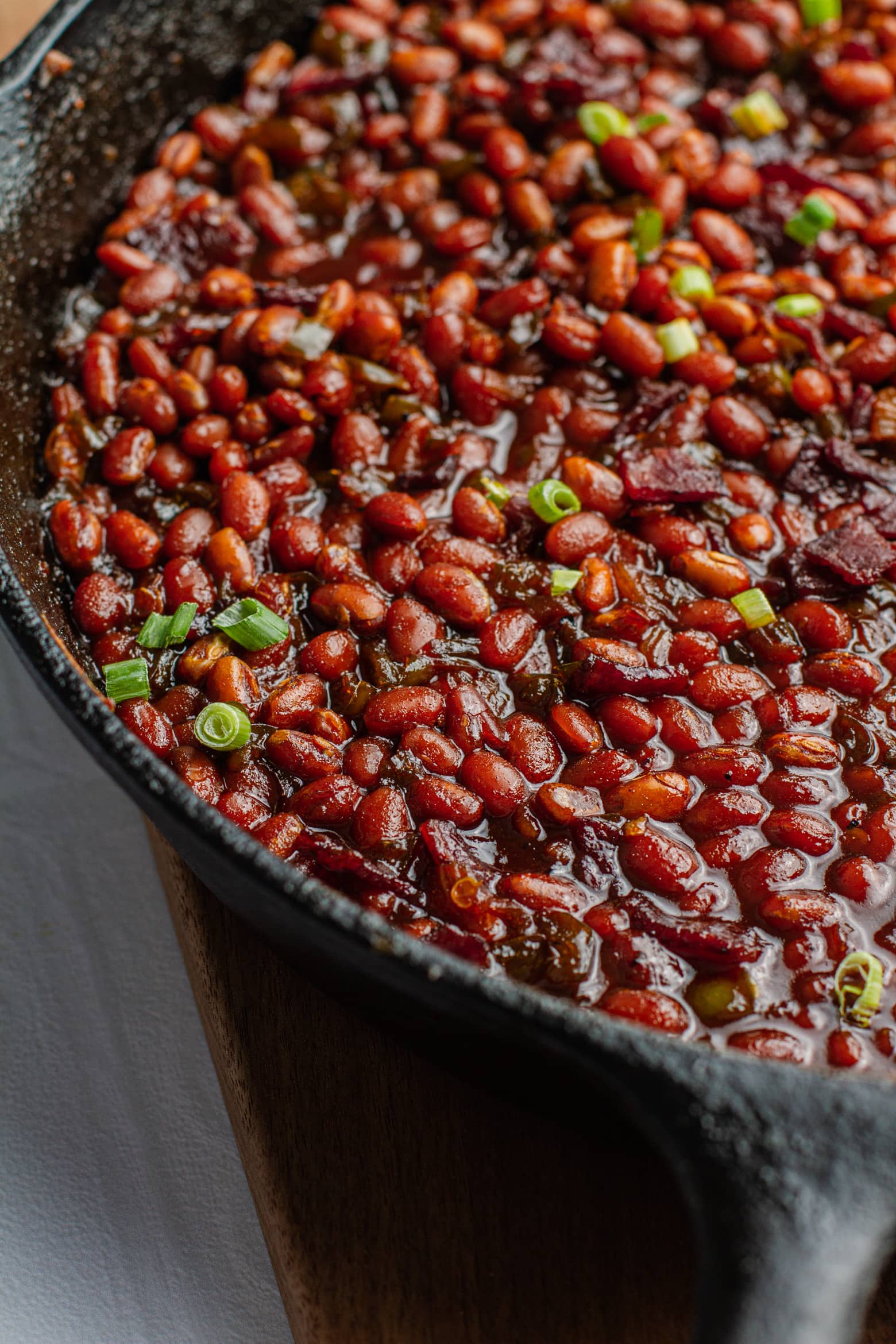 close up of Southern brown sugar baked beans in a cast iron pan on a wooden cutting board