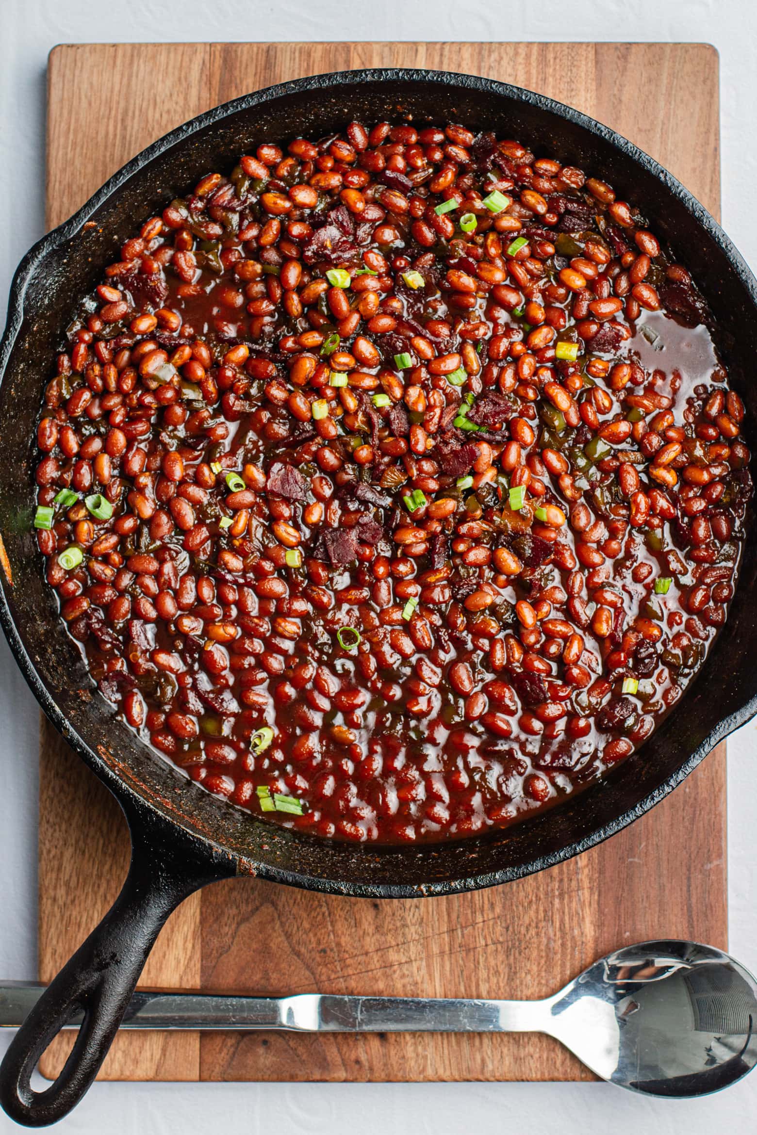 Southern brown sugar baked beans in a cast iron pan on a wooden cutting board with a spoon