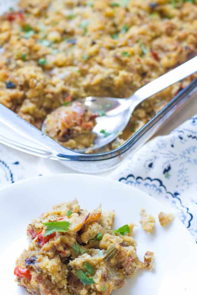 Close up view of small white plate with Home-style Turkey Stuffing placed next to a pyrex pan of full of the stuffing and a spoon sitting in the pan.