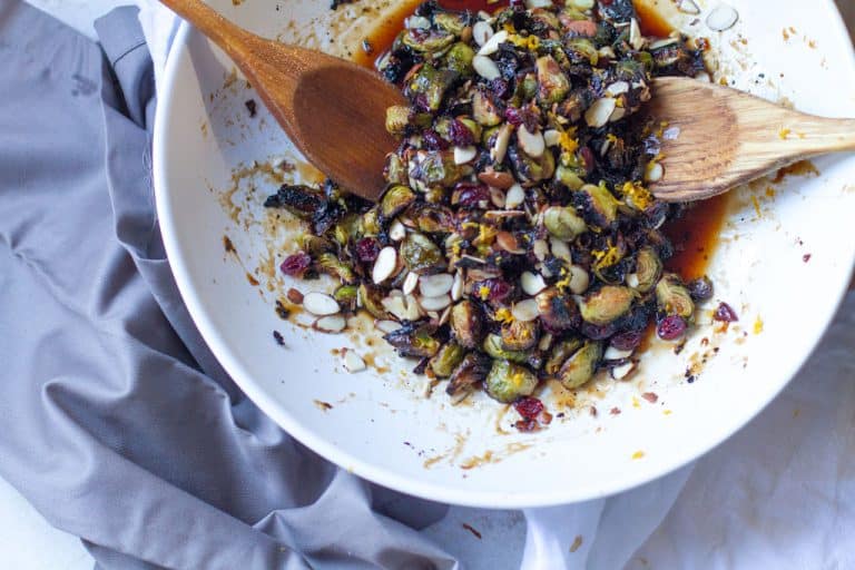 Aerial view of the vegan candied Brussels sprouts in a white bowl with 2 wooden spoons.