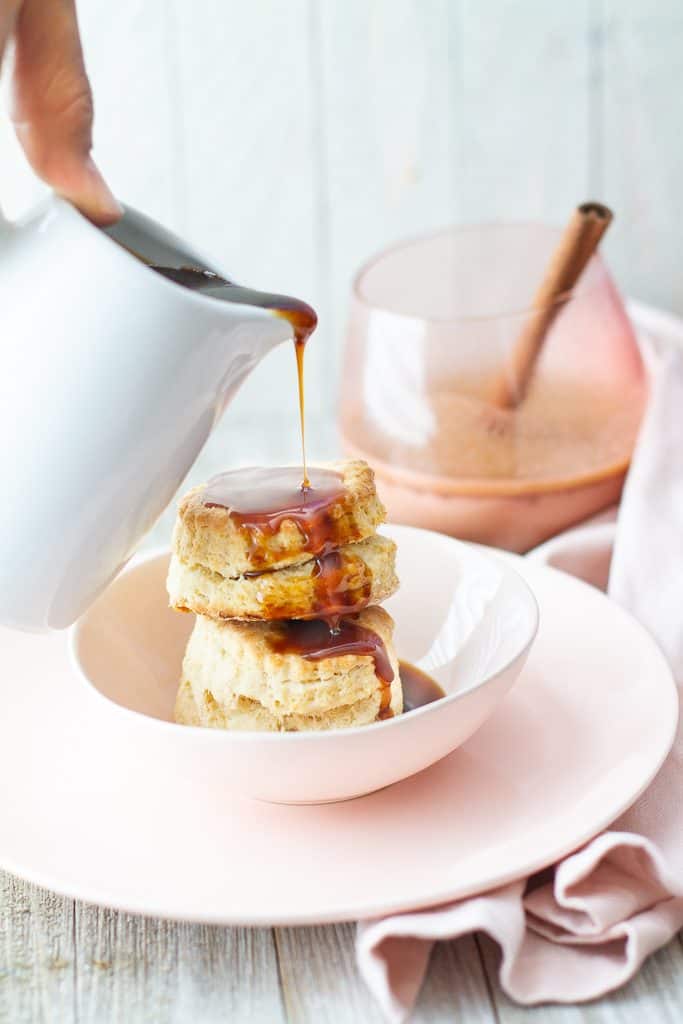 Two biscuits in saucer with a drizzle of hot butter rum sauce. In front of a hot buttered rum cocktail