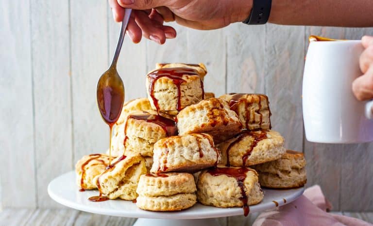 Spoon in hand pouring hot buttered rum sauce across buttermilk biscuits.