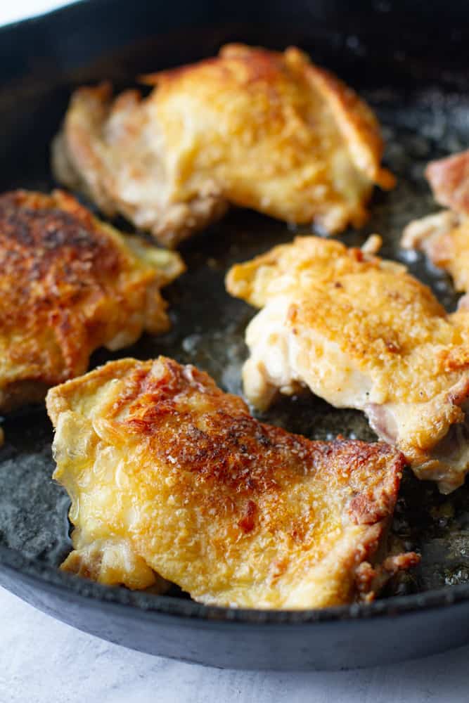 Close up shot of chicken thighs being friend in cast iron skillet.