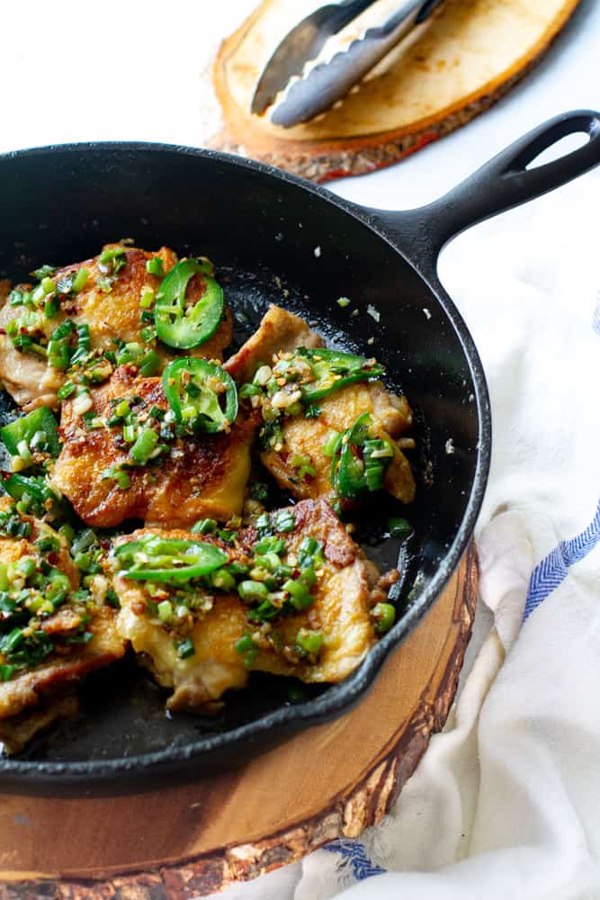 Salt and pepper chicken thighs displayed in cast iron skillet.