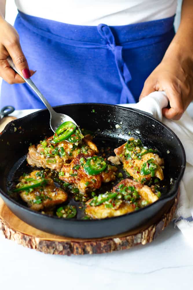 Shot of salt and pepper chicken thighs displayed in cast iron skillet with hand adding topping.