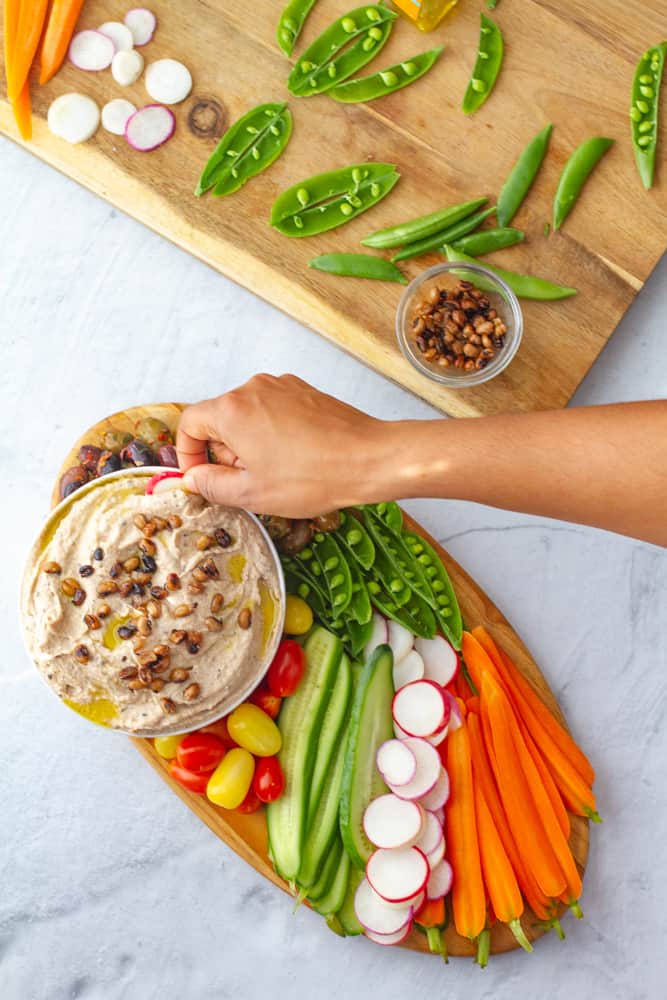 Black eyed Pea Hummus with platter of vegetables and hand reaching in to dip vegetable in hummus.