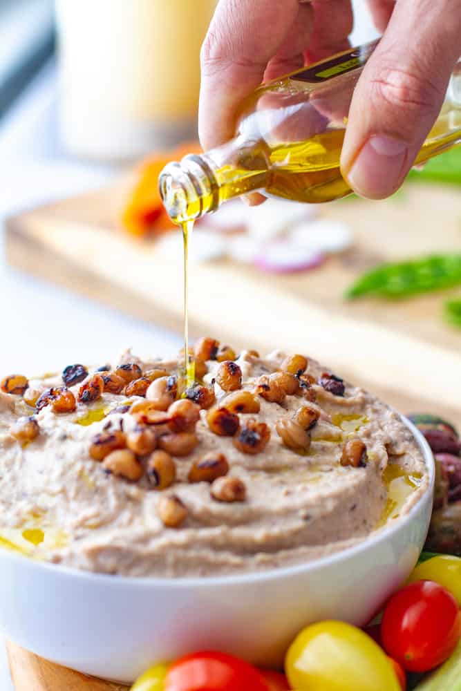 Black eyed Pea Hummus with platter of vegetables and hand pouring olive oil on top