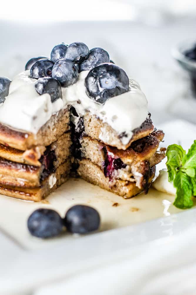 Cut into a stack of Blueberry Lemon Keto Pancakes topped whipped cream and fresh blueberries.