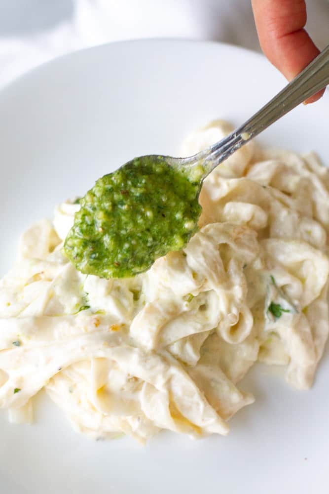 Spooning pesto sauce on top of Fettuccine Alfredo with low carb shirataki noodles.