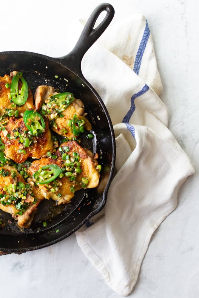 Aerial shot of salt and pepper chicken thighs displayed in cast iron skillet.