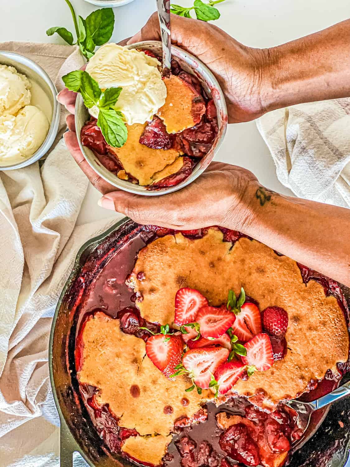 Meiko holding a bowl of Strawberry Cornbread Skillet Cobbler topped with ice cream and garnish with mint leaves.