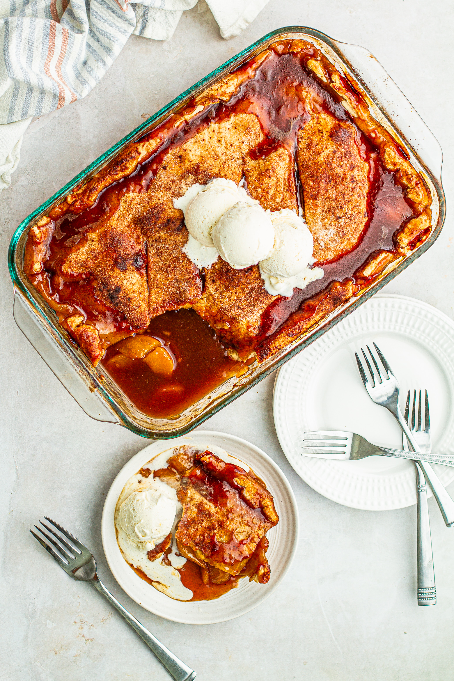 soul food peach cobbler canned peaches on a plate with a scoop of vanilla ice cream and a baking dish with three scoops of vanilla ice cream