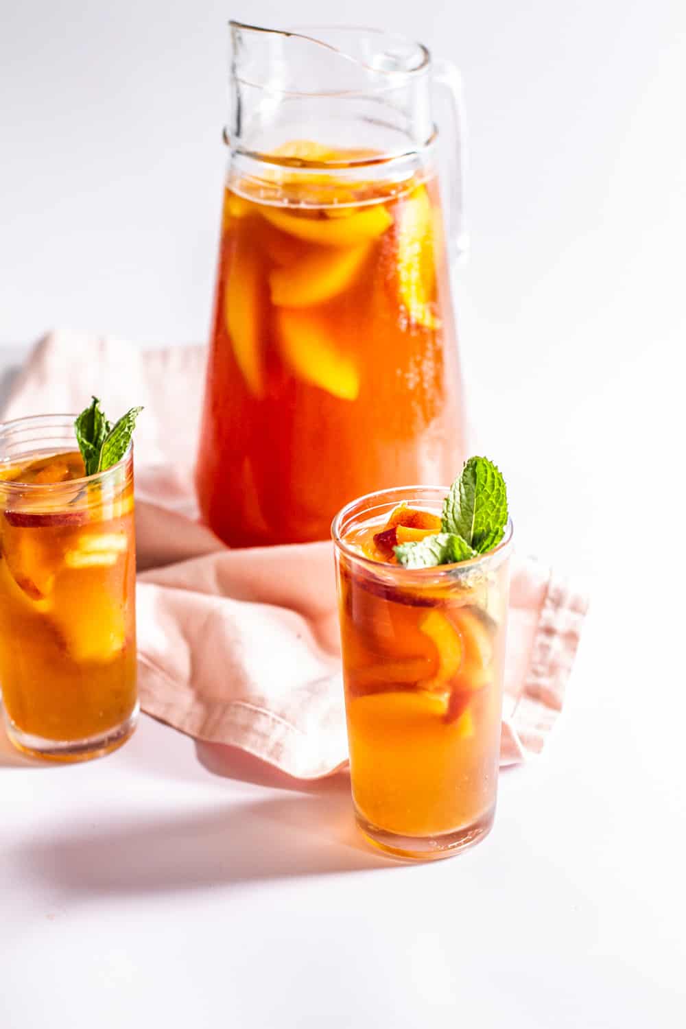a pitcher and two glasses of Peach Sweet Tea garnished with mint leaves