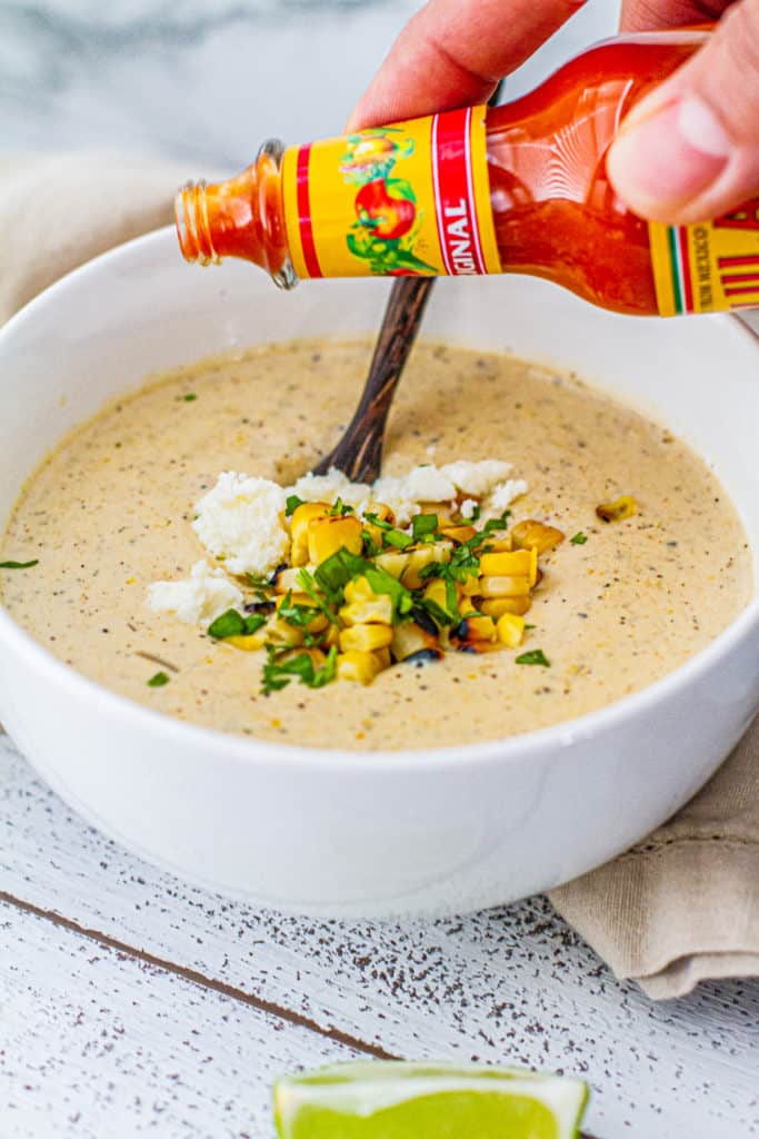 Pouring hot sauce on elote corn chowder in a bowl