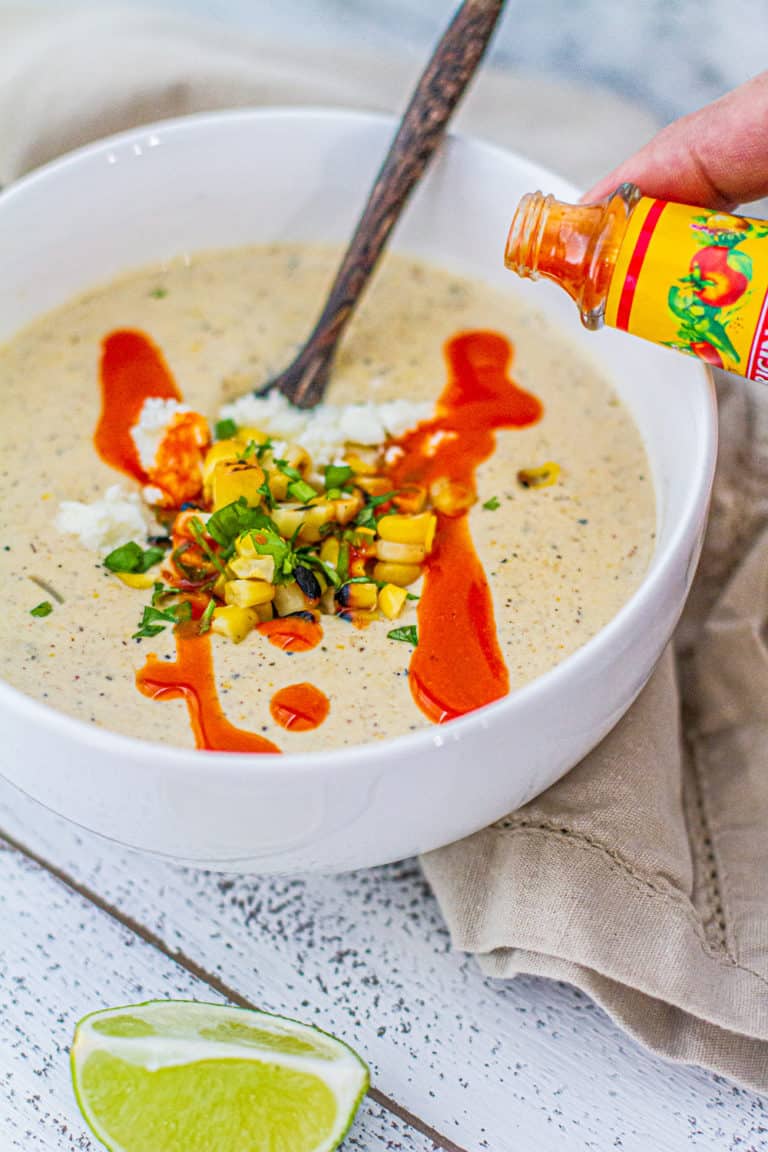 pouring hot sauce on elote corn chowder