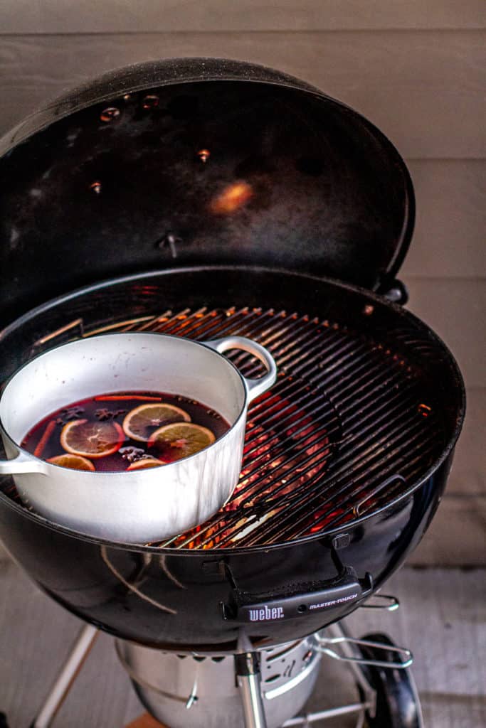white pot on grill with mulled wine and fruit inside