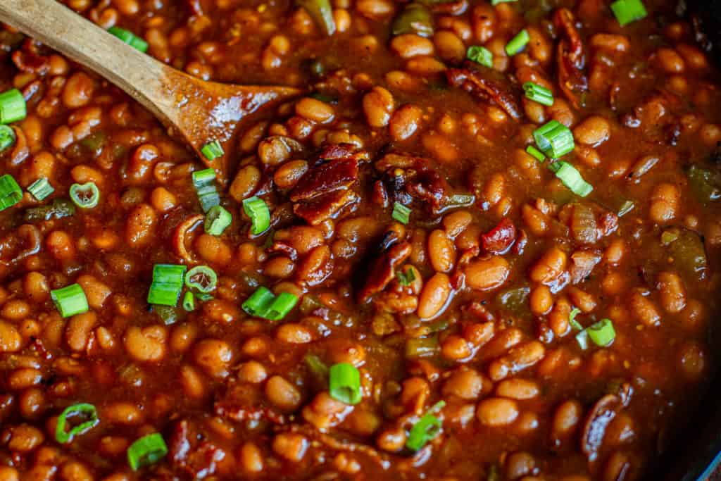 close up baked beans in cast iron with wooden spoon