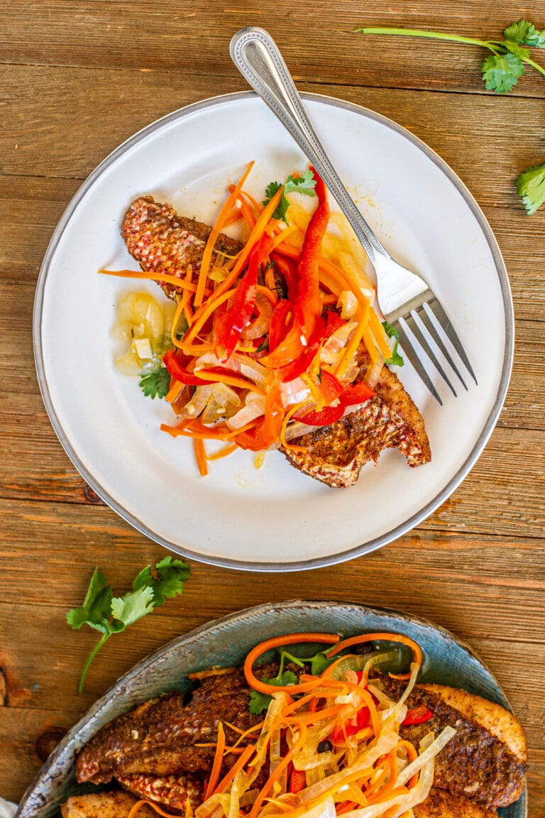 Overhead shot Escovitch snapper on white plate with pickled onions and bell peppers