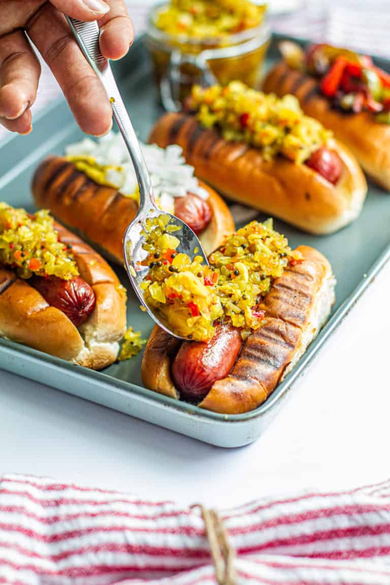 This is a recipe for chow chow and grilled hot links. It shows how to make grilled hot links & homemade chow chow. A hand is adding Southern chow chow relish to hot link on a grilled bun for a Juneteenth celebration..