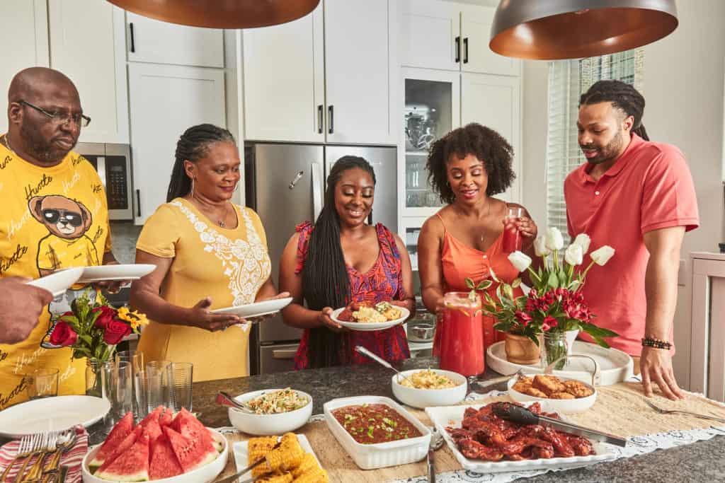 Meiko & Kenneth in the kitchen will family in front of a large spread of Juneteenth foods.