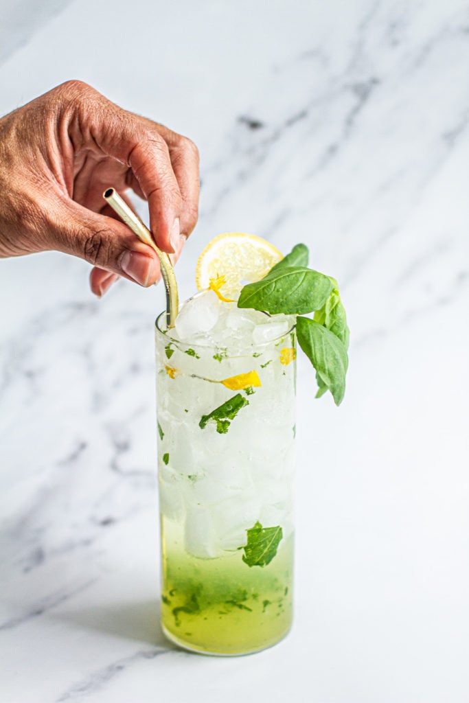 hand placing staw in cup of lemon basil mojito