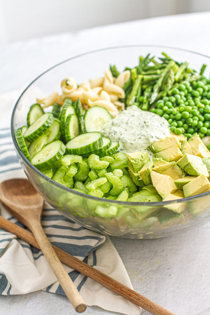 large bowl with celery, cucumber, avocado, peas, and pasta for green goddess pasta salad