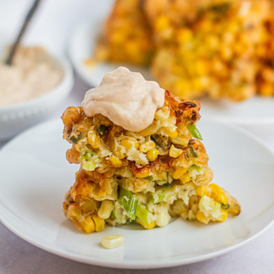 3 corn fritters stacked on plate with dollop of herb crema on top