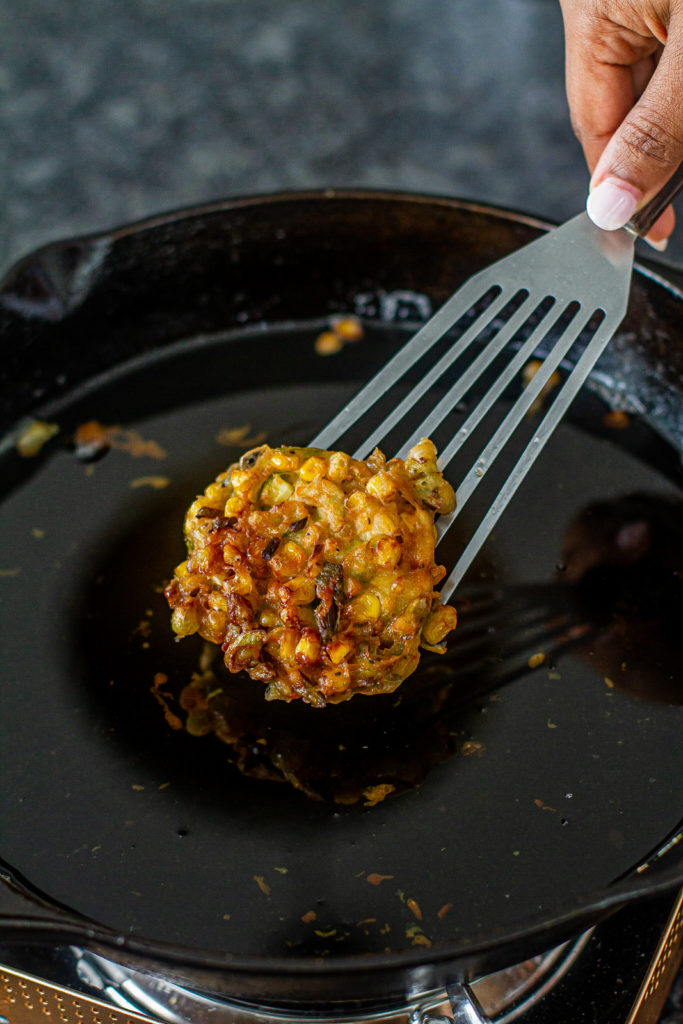 a corn fritter being fried in a skillet with a spatula
