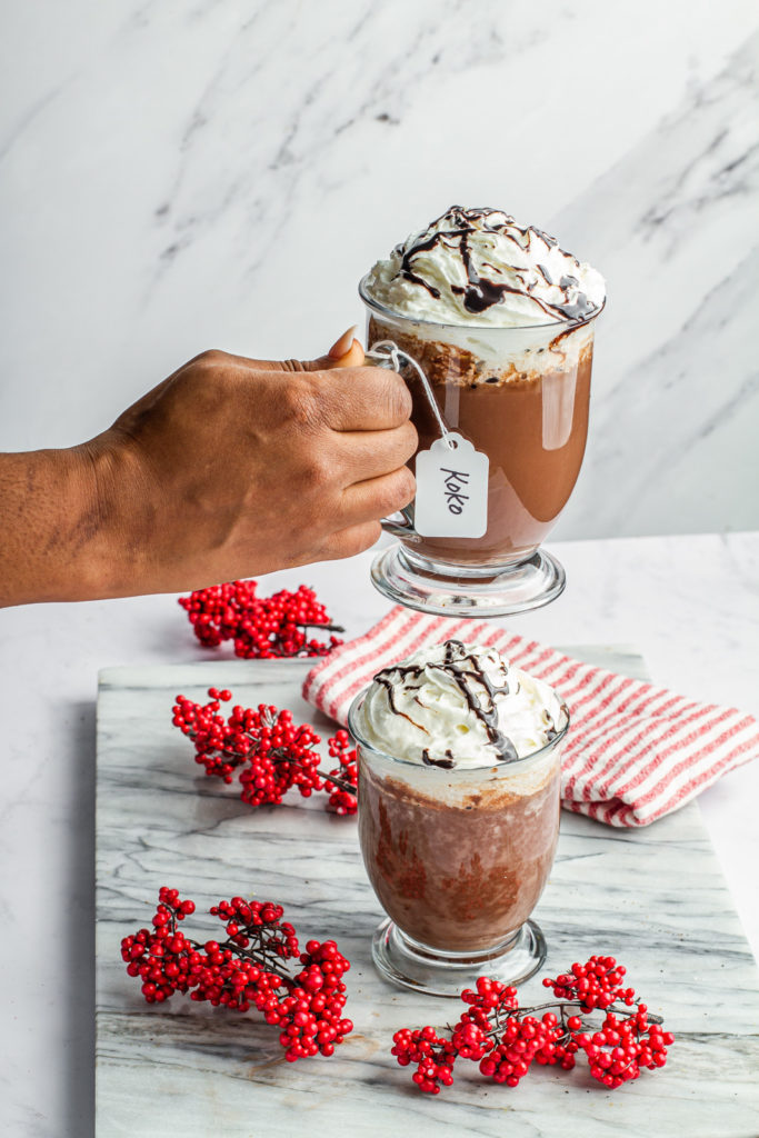 hand holding, red wine hot chocolate topped with whip cream and chocolate drizzle in mug