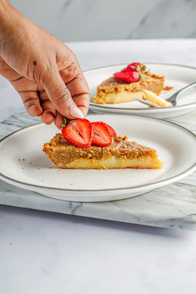 hand placing strawberries on slice of goat milk pie