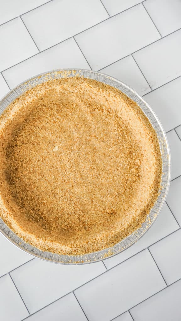 overhead shot of graham cracker crust pressed into a pie tin on counter