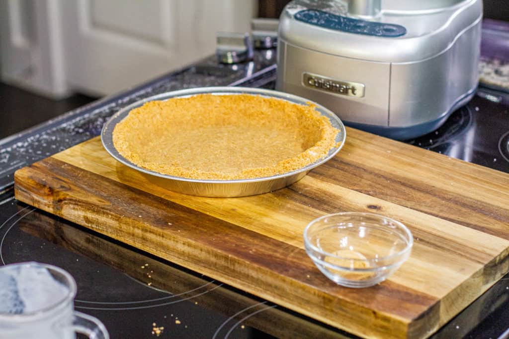 graham cracker crust pressed into a pie tin on a wooden chopping board