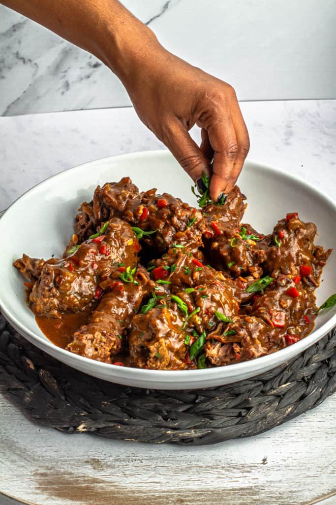 meiko's hand garnishing smothered turkey necks with gravy on a platter