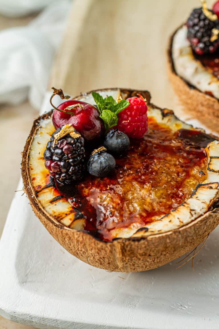 closeup of sombi brown butter rice pudding brulee garnished with blueberries raspberries cherries blackberries and mint on a decorative cutting board