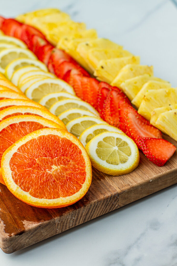 sliced oranges, lemons, strawberries, and pineapples on a wooden cutting board