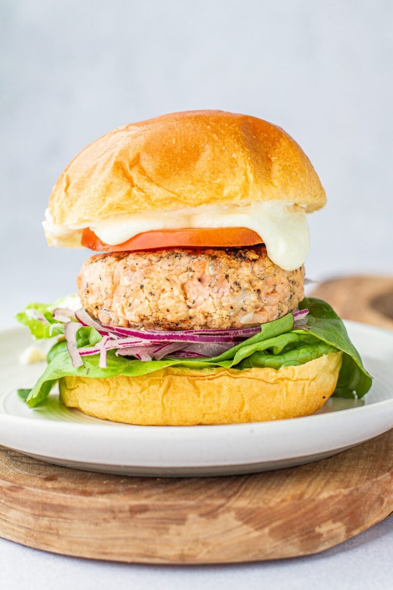 close up of fresh salmon burger on a plate on a wooden cutting board