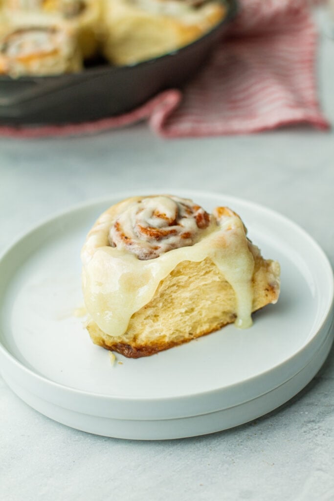 one buttermilk cinnamon roll on plate with frosting melted down the sides