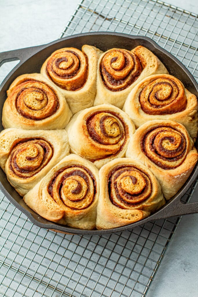 warm cinnamon rolls in cast iron resting and cooling on baking rack