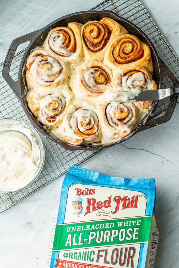 buttermilk cinnamon rolls in cast iron with frosting next to flour