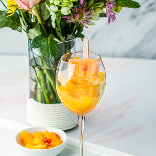 Tropical Moscato Poptail in a glass on a serving tray with a side of peaches and a bouquet of flowers