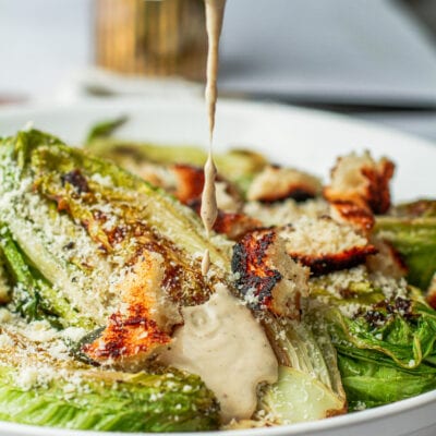 of the best grilled Caesar salad on a platterouring creamy caesar dressing on the best grilled Caesar salad in a bowl