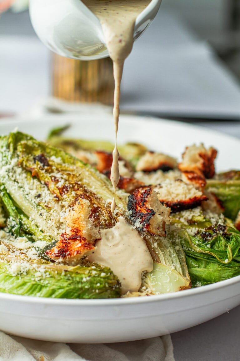 of the best grilled Caesar salad on a platterouring creamy caesar dressing on the best grilled Caesar salad in a bowl